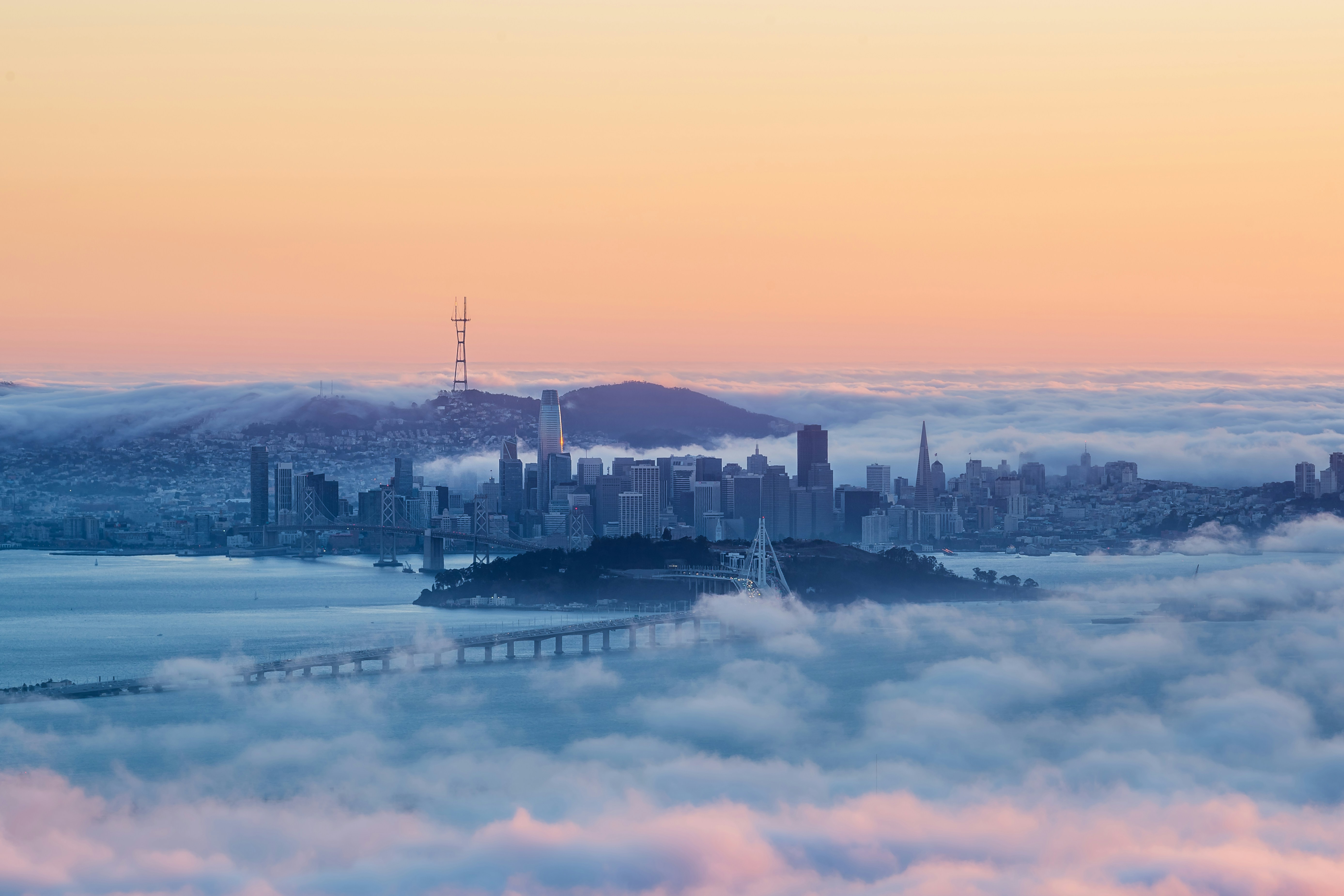San Francisco seen from above, its skyline rising out of a blanket of fog in golden light